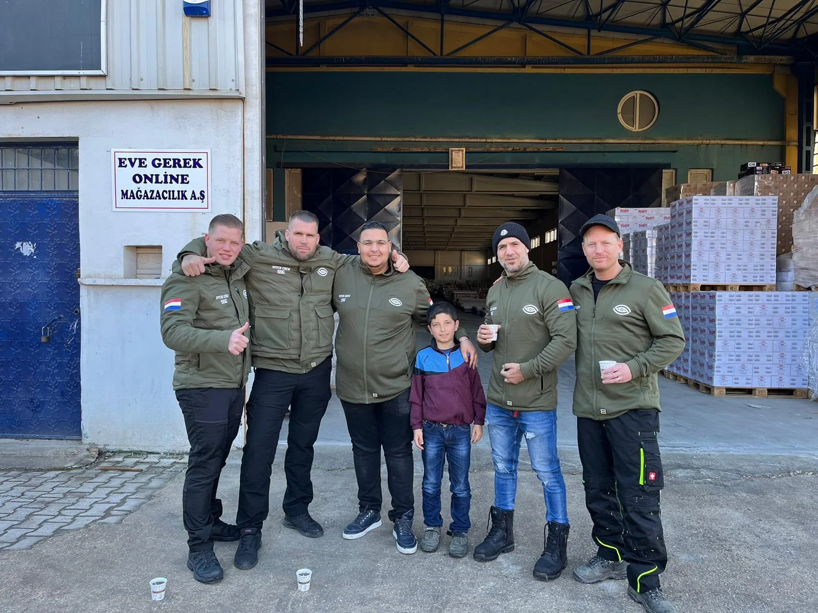 Team van SSG in hulpverleningstenue bij het magazijn in Turkije, samen met een jongen uit de buurt