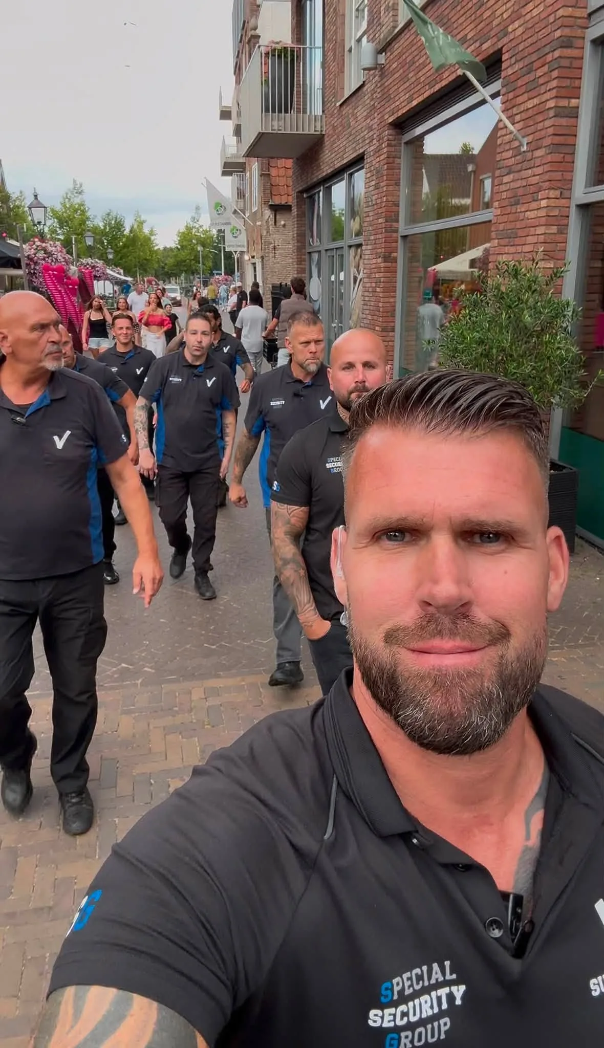 Beveiliger maakt een selfie terwijl zijn team achter hem door de winkelstraat loopt tijdens de feestweek
