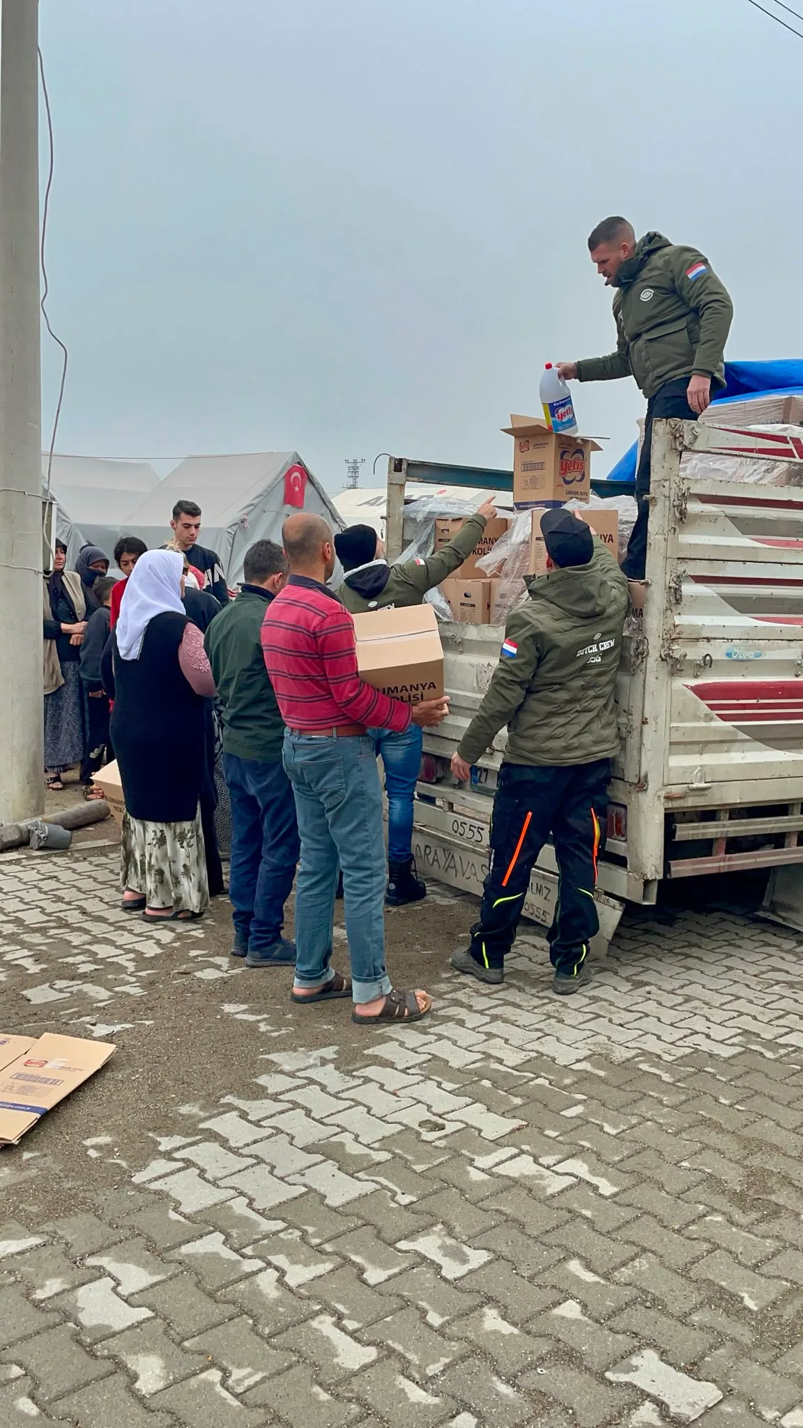 Medewerkers van SSG delen voedselpakketten uit vanaf een vrachtwagen aan bewoners bij een tentenkamp