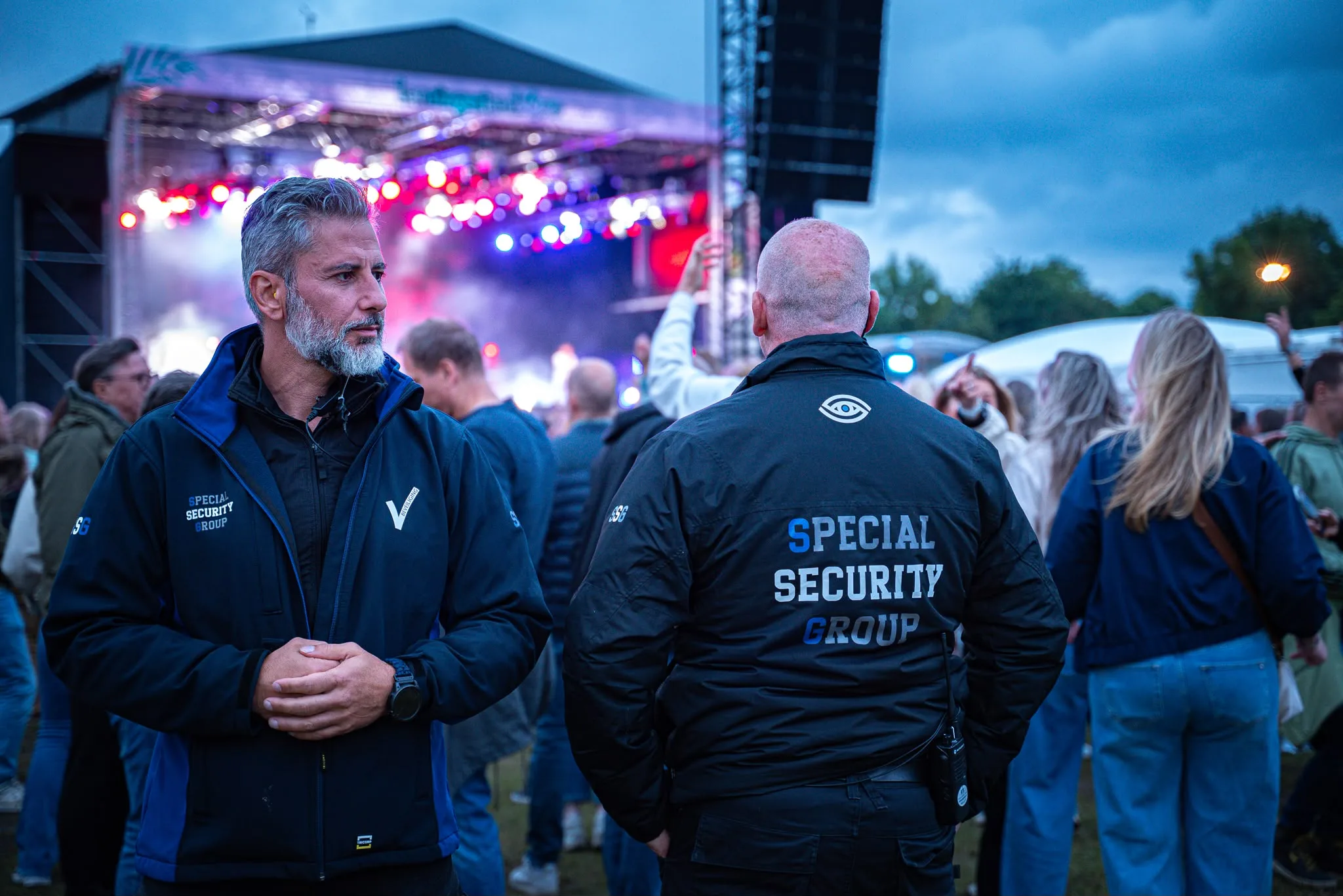 Twee beveiligers van SSG overleggen tussen het publiek terwijl het podium achter hen speelt