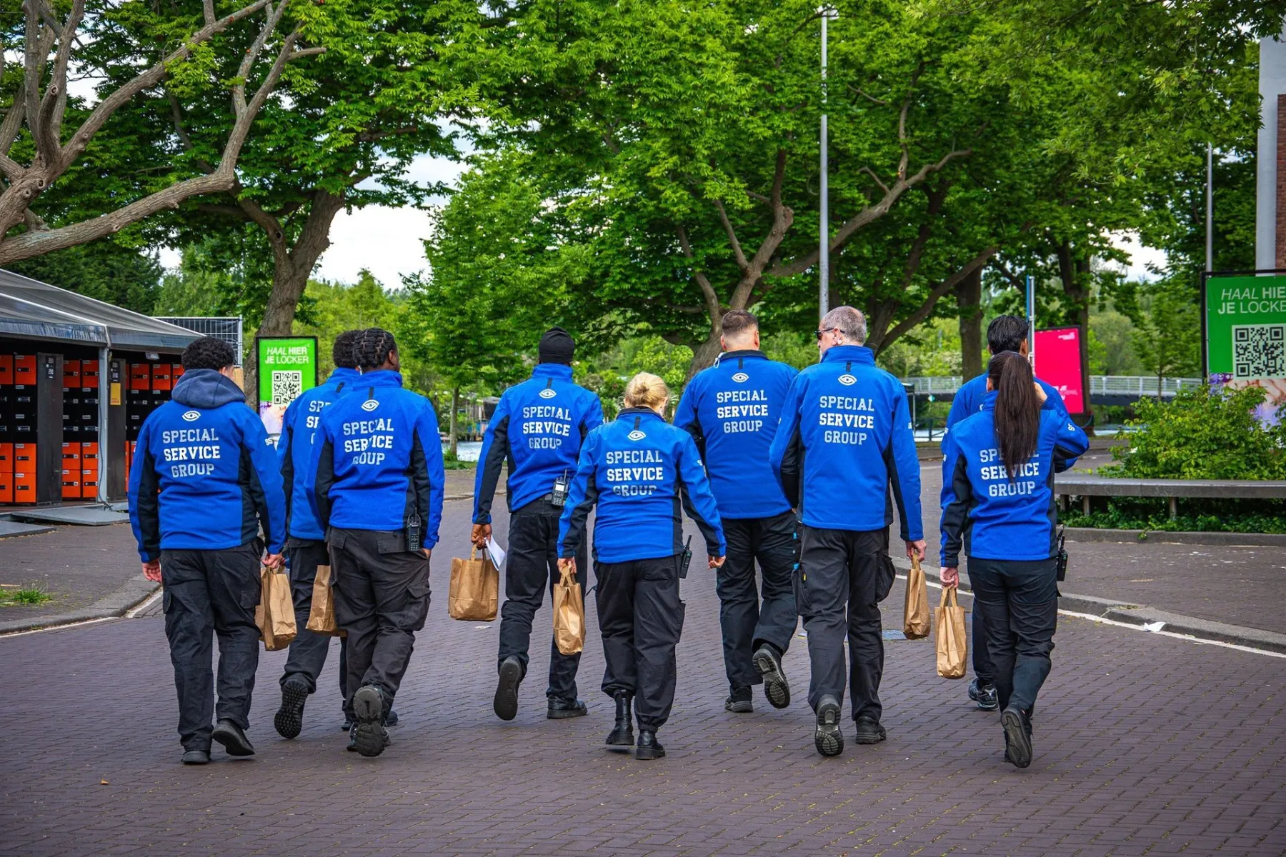 Servicemedewerkers in blauwe jassen van Special Service Group lopen met bestellingen over een evenemententerrein