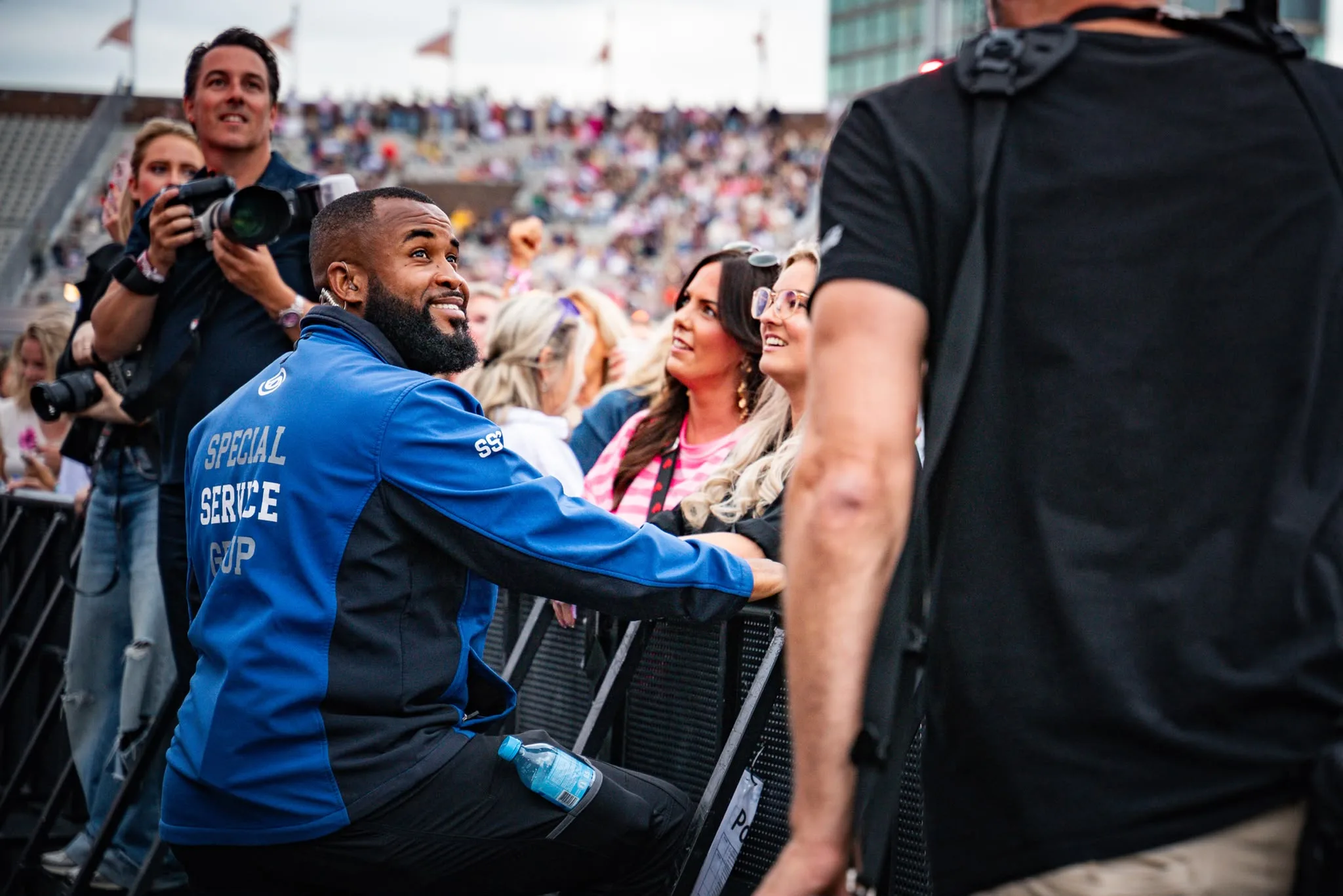 Servicemedewerker van Special Service Group maakt een praatje met bezoekers aan de barrier in een stadion