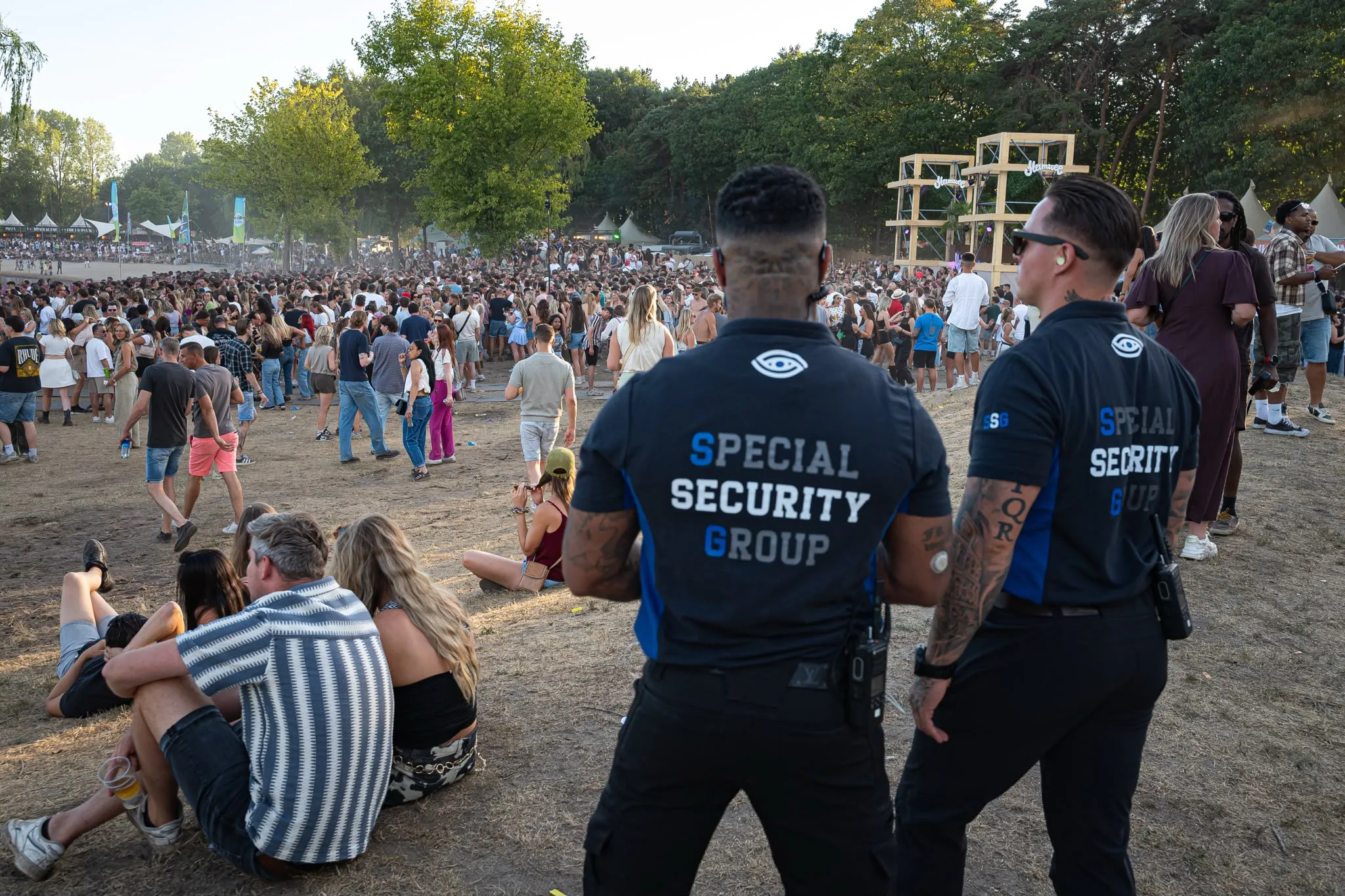 Twee beveiligers van SSG overleggen tussen het publiek terwijl het podium achter hen speelt
